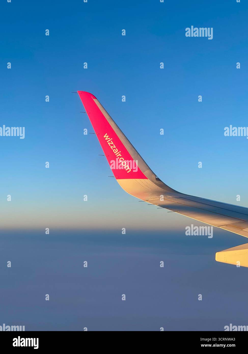La vista dalla finestra dell'aeroplano mostra la punta dell'ala di Wizz Air contro un cielo sereno, catturando la calma bellezza del marchio di volo e dei viaggi economici Foto Stock