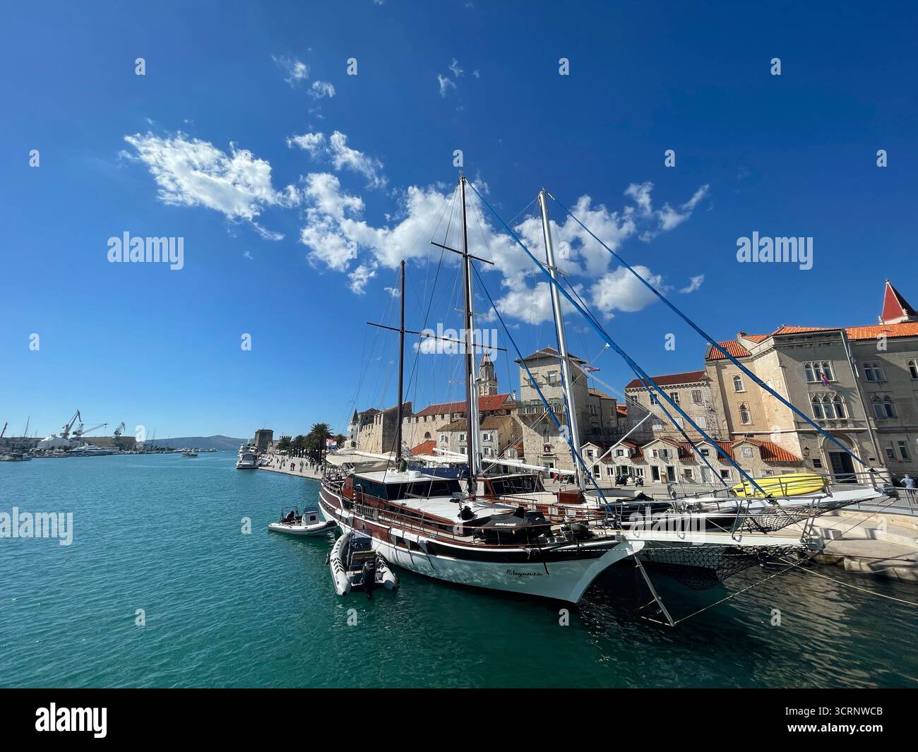 Yacht a vela ormeggiato nel porto di Traù, in Croazia, con edifici storici della città vecchia e torre della chiesa sotto un cielo azzurro dell'Adriatico Foto Stock