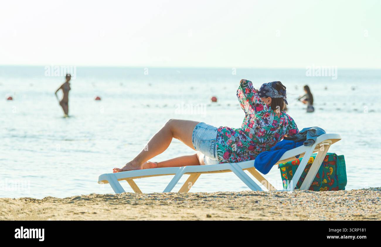 una donna vestita giace su un lettino di plastica da spiaggia Foto Stock