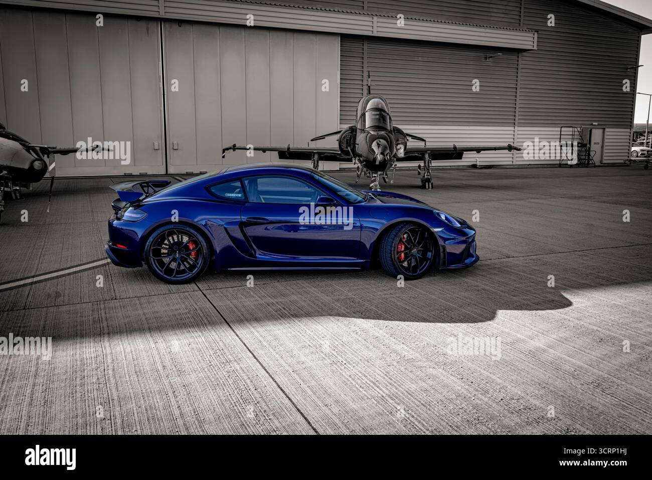 Auto sportiva Blue Porsche sull'asfalto gallese della base RAF con jet RAF Hawk sullo sfondo durante un soleggiato evento motoristico britannico di settembre Foto Stock