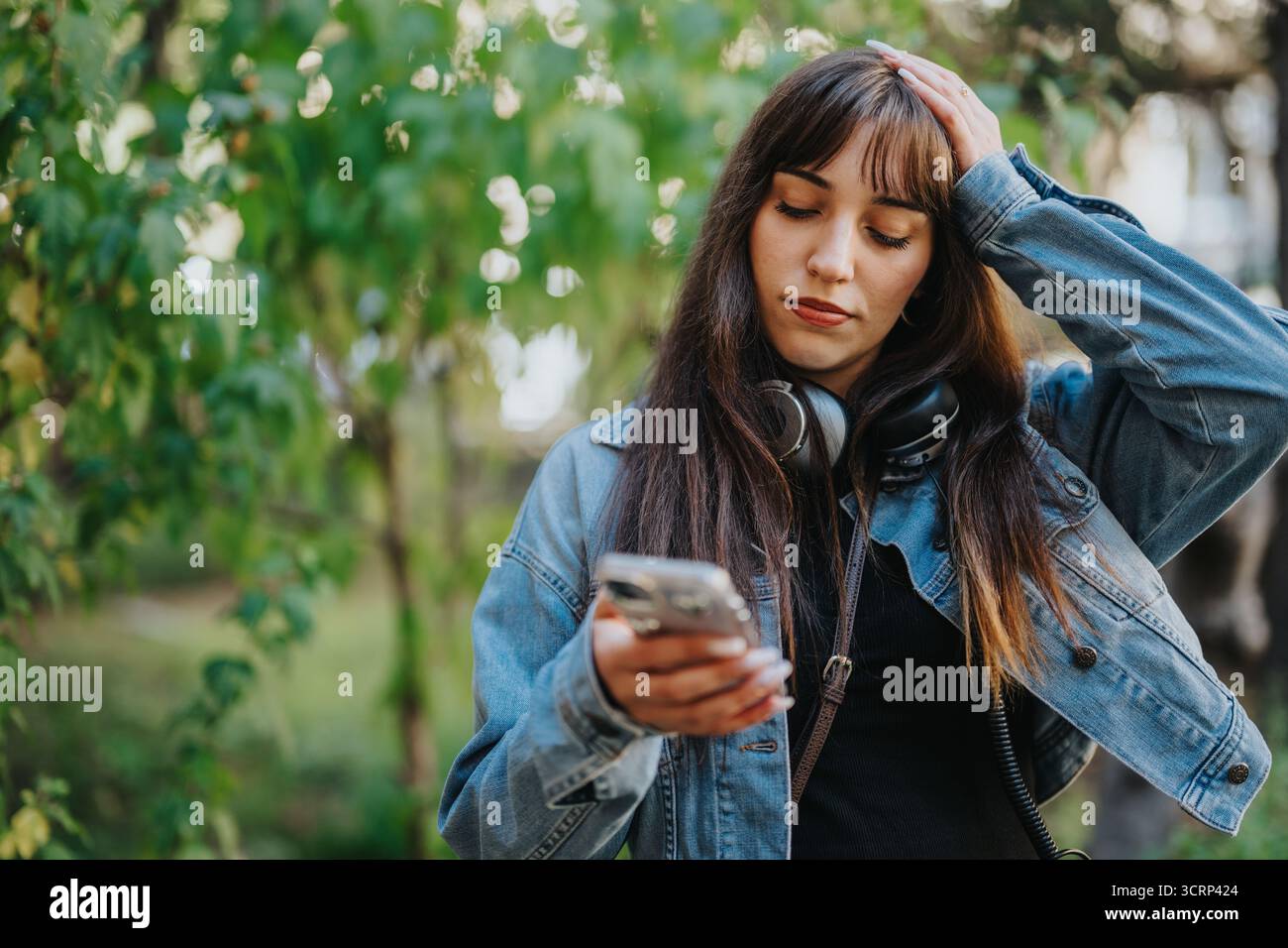 Giovane donna con giacca in denim che tiene il telefono all'aperto in una giornata di sole Foto Stock