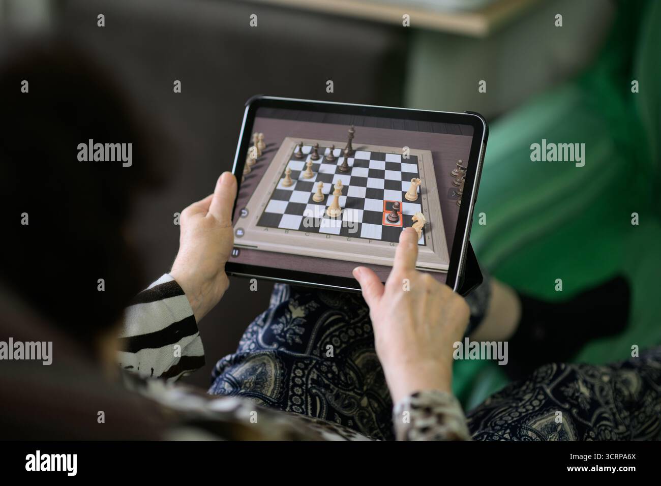 Una donna anziana utilizza un tablet per spostare i pezzi degli scacchi su una tavola virtuale, esercitando strategia digitale e capacità di memoria che supportano la salute cognitiva, foc Foto Stock