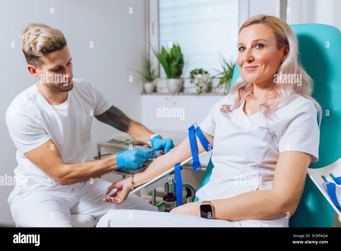 Un operatore sanitario sta prelevando sangue da un paziente sorridente in un ambiente medico pulito. Foto Stock