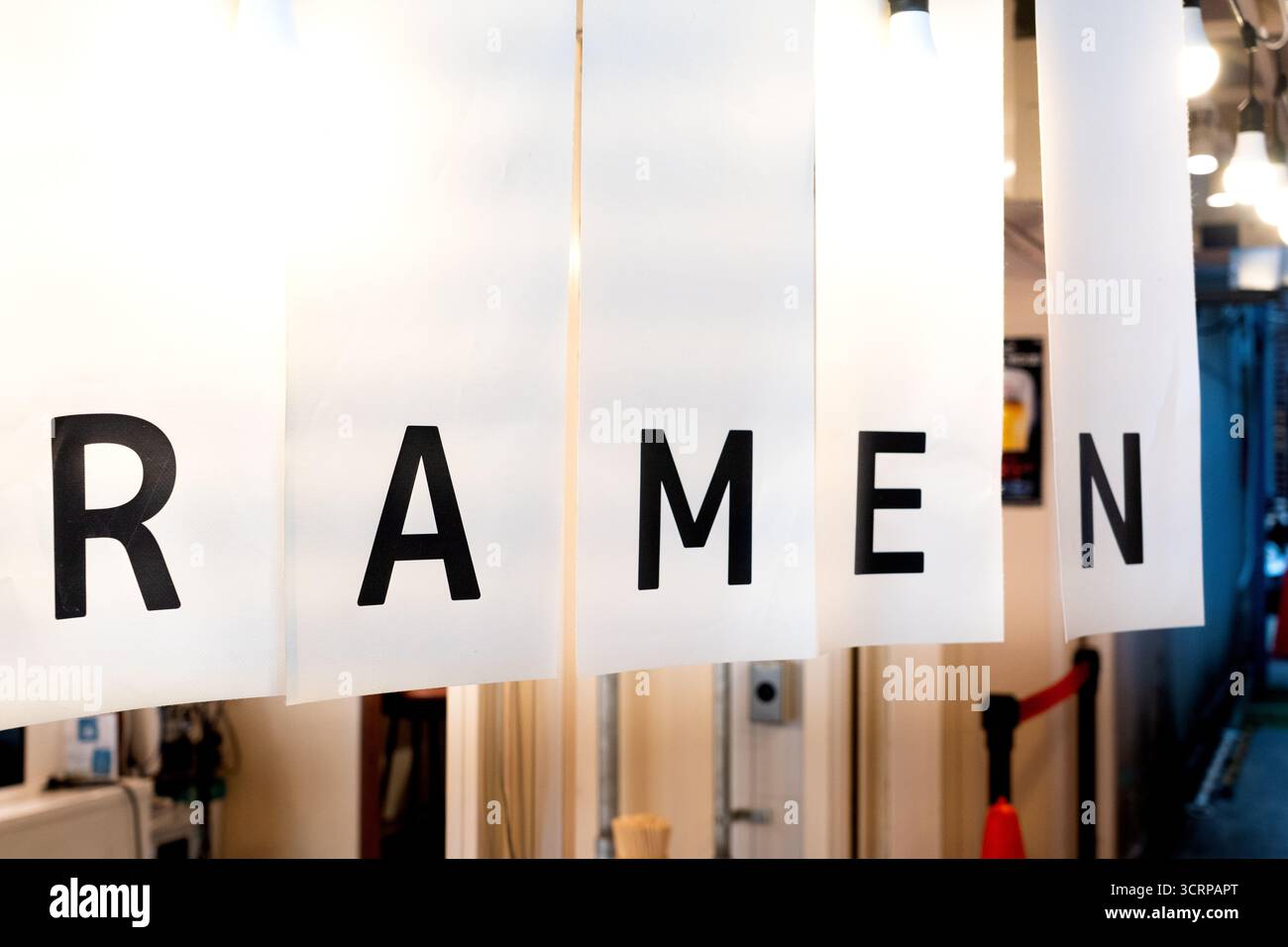 Tenda noren bianca minimalista con audaci lettere nere che scrivono "RAMEN" appese all'ingresso di un tradizionale negozio di ramen giapponese. Foto Stock
