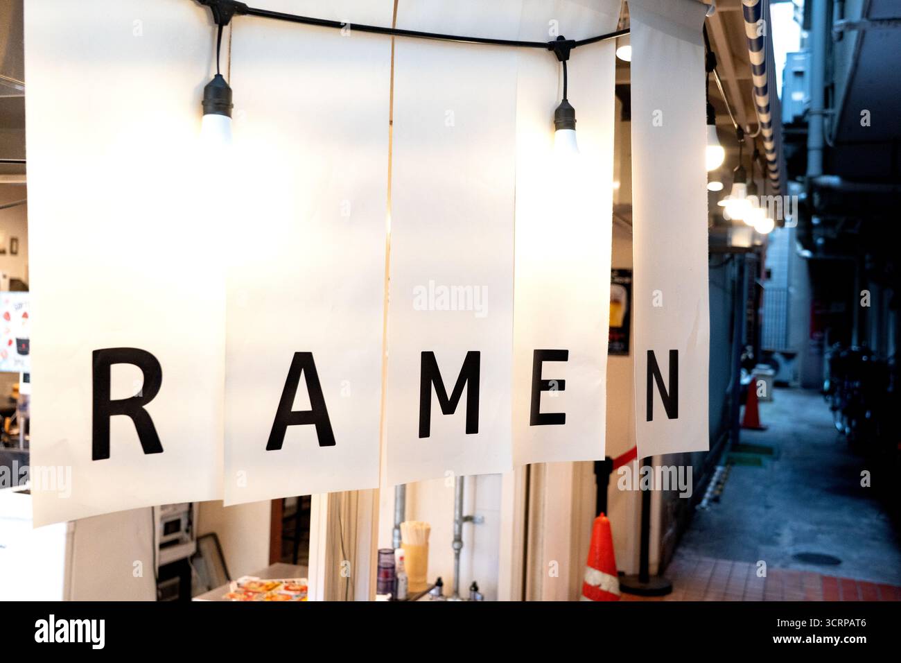 Tenda noren bianca minimalista con audaci lettere nere che scrivono "RAMEN" appese all'ingresso di un tradizionale negozio di ramen giapponese. Foto Stock