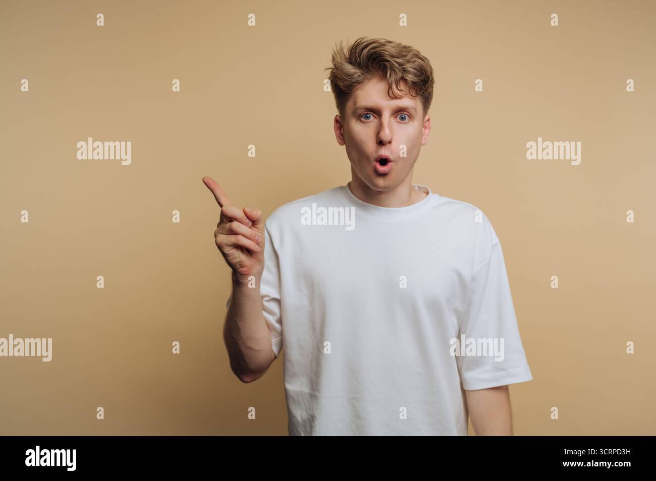Un giovane con i capelli ruvidi sta esprimendo eccitazione, alzando un dito e mostrando un'espressione facciale sorpreso su uno sfondo semplice. Il suo W Foto Stock