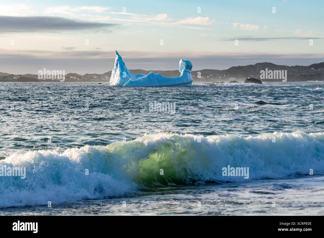 Un'onda si schianta sulla riva di fronte a un iceberg. Foto Stock