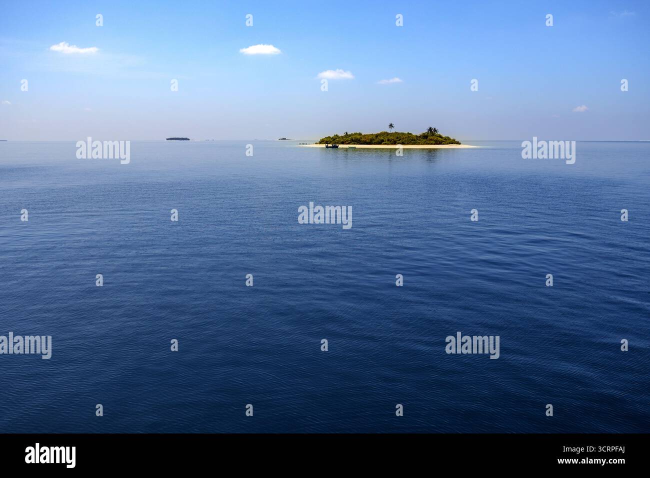 Una vista serena di una piccola isola tropicale circondata da calme acque blu sotto un cielo limpido, che mostra la bellezza naturale e la tranquillità di un islan Foto Stock