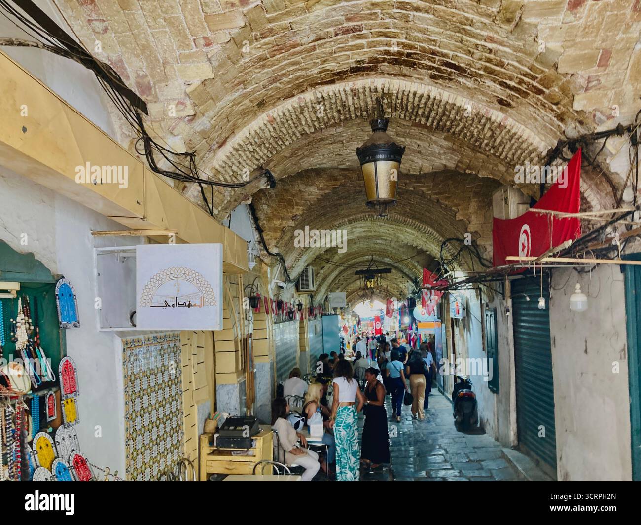 Vicolo coperto di suk nella vecchia Medina vicino a Bab El Bhar, Tunisi, Tunisia: Soffitto a volta in mattoni, lanterne e vita di mercato. Catturato il 24 settembre 2025. Foto Stock