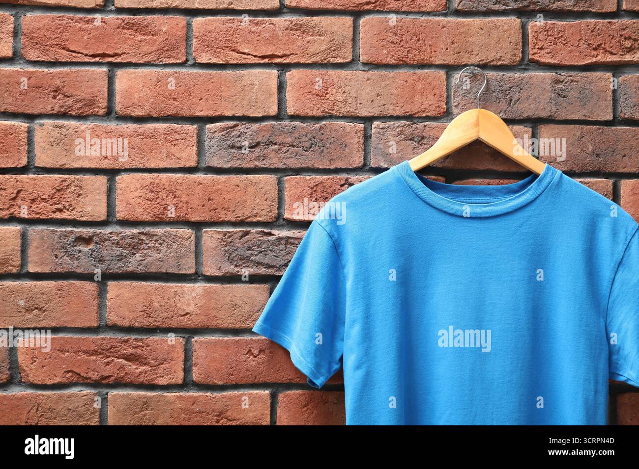 Appendiabiti con t-shirt azzurra contro il muro di mattoni rossi, primo piano. Mockup per il design Foto Stock