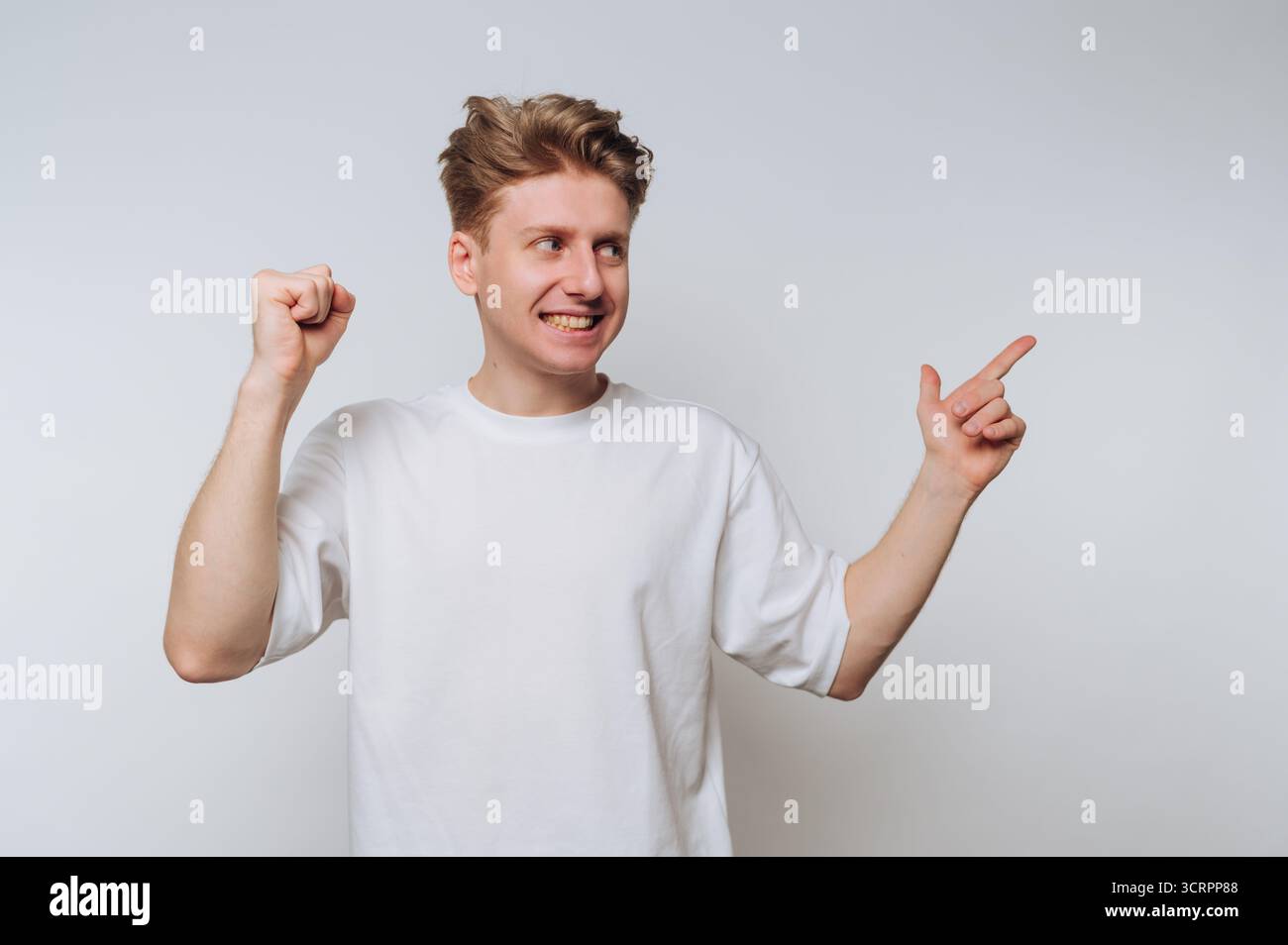 Giovane uomo con t-shirt bianca che punta e sorride su sfondo bianco. Foto Stock
