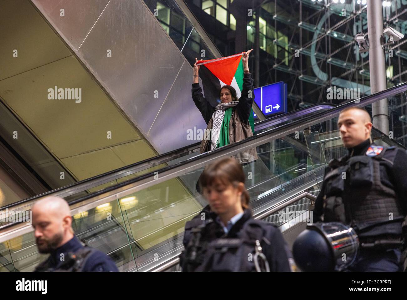 Protesta für Gaza und Solidartät mit der Sumud Flotilla am Berliner Hauptbahnhof. AM Berliner Hauptbahnhof. Deutschland, Berlin am 01.10.2025: Junge Aktivistin hält eine Palästina-Fahne hoch über sich, als sie nach Beendigung der Demonstration neben Polizistinnen und Polizisten auf der Rolltreppe im Hauptbahnhofgebäude fährt. Bis spät in Die Nacht haben Menschen ihre Solidarität mit der Sumud Flotilla am Berliner zentralen Hauptbahnhof ausgedrückt. Gegen 23:30 Hat die Polizei die Demo für beendet erklärt. *** Protesta per Gaza e solidarietà con la flottiglia Sumud alla stazione centrale di Berlino a B. Foto Stock