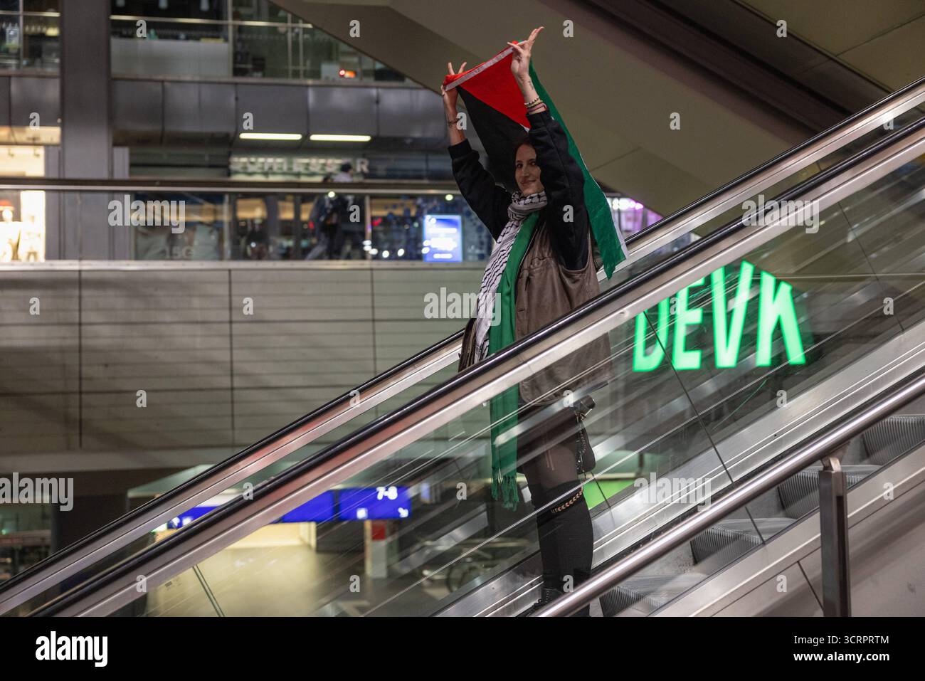Protesta für Gaza und Solidartät mit der Sumud Flotilla am Berliner Hauptbahnhof. AM Berliner Hauptbahnhof. Deutschland, Berlin am 01.10.2025: Junge Aktivistin hält eine Palästina-Fahne hoch über sich, als sie nach Beendigung der Demonstration auf der Rolltreppe im Hauptbahnhofgebäude fährt. Bis spät in Die Nacht haben Menschen ihre Solidarität mit der Sumud Flotilla am Berliner zentralen Hauptbahnhof ausgedrückt. Gegen 23:30 Hat die Polizei die Demo für beendet erklärt. *** Protesta per Gaza e solidarietà con la Flottiglia Sumud alla stazione centrale di Berlino alla stazione centrale di Berlino Germania, Berl Foto Stock