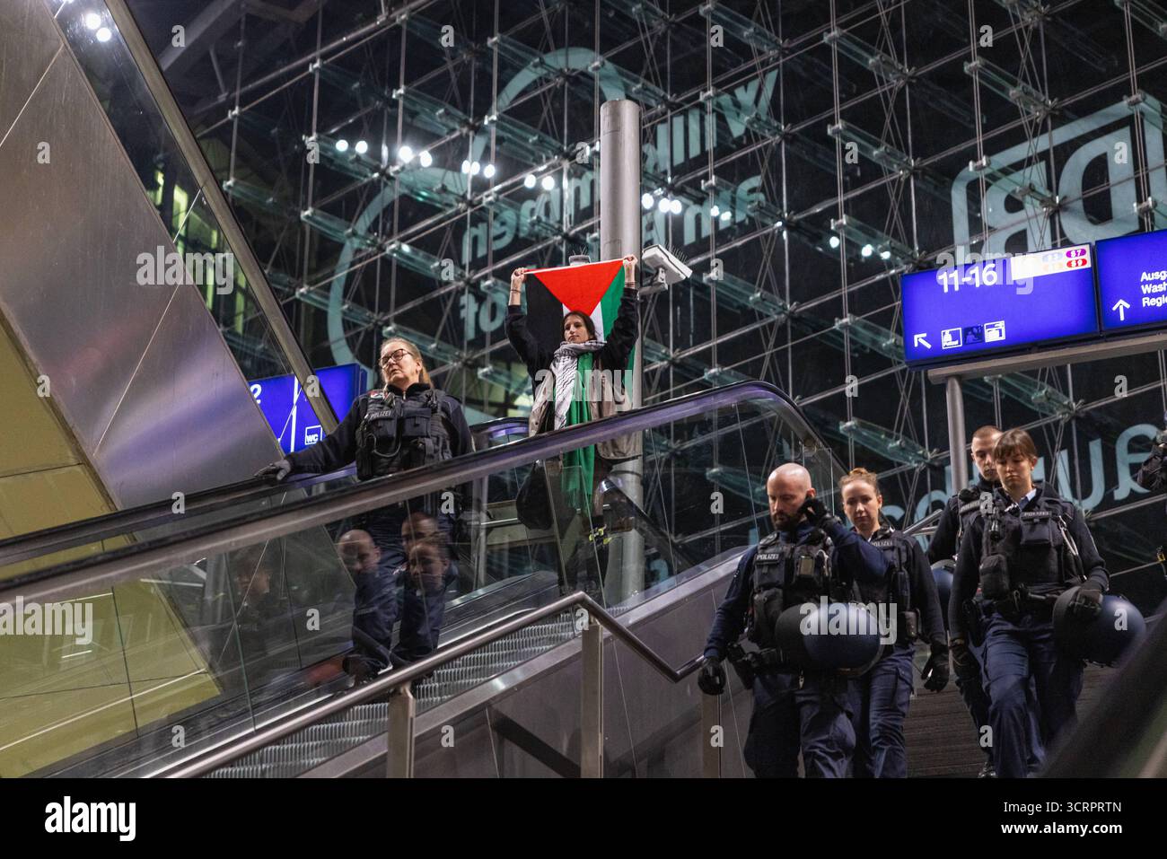 Protesta für Gaza und Solidartät mit der Sumud Flotilla am Berliner Hauptbahnhof. AM Berliner Hauptbahnhof. Deutschland, Berlin am 01.10.2025: Junge Aktivistin hält eine Palästina-Fahne hoch über sich, als sie nach Beendigung der Demonstration neben Polizistinnen und Polizisten auf der Rolltreppe im Hauptbahnhofgebäude fährt. Bis spät in Die Nacht haben Menschen ihre Solidarität mit der Sumud Flotilla am Berliner zentralen Hauptbahnhof ausgedrückt. Gegen 23:30 Hat die Polizei die Demo für beendet erklärt. *** Protesta per Gaza e solidarietà con la flottiglia Sumud alla stazione centrale di Berlino a B. Foto Stock