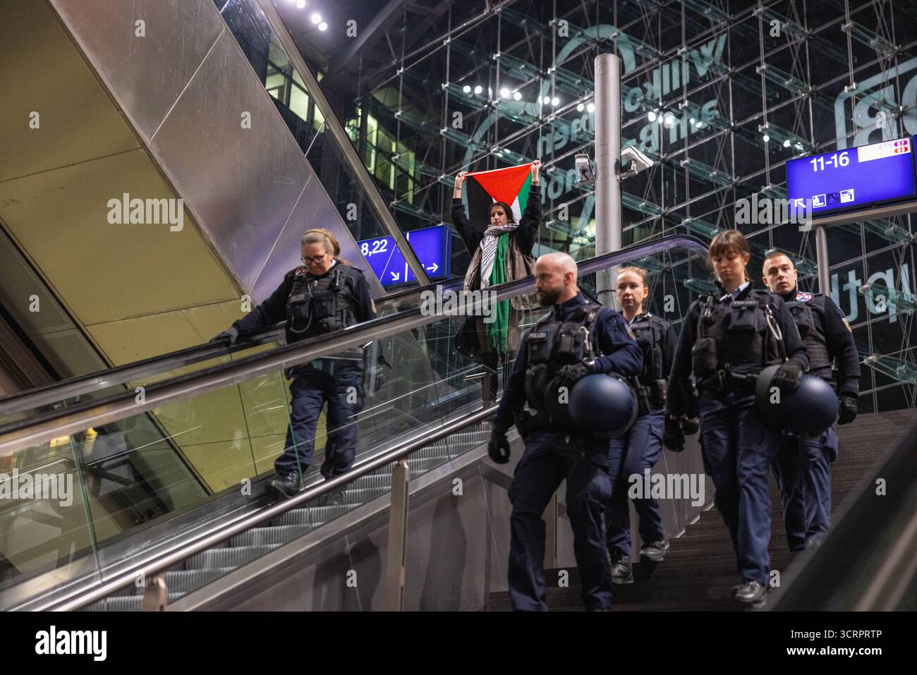 Protesta für Gaza und Solidartät mit der Sumud Flotilla am Berliner Hauptbahnhof. AM Berliner Hauptbahnhof. Deutschland, Berlin am 01.10.2025: Junge Aktivistin hält eine Palästina-Fahne hoch über sich, als sie nach Beendigung der Demonstration neben Polizistinnen und Polizisten auf der Rolltreppe im Hauptbahnhofgebäude fährt. Bis spät in Die Nacht haben Menschen ihre Solidarität mit der Sumud Flotilla am Berliner zentralen Hauptbahnhof ausgedrückt. Gegen 23:30 Hat die Polizei die Demo für beendet erklärt. *** Protesta per Gaza e solidarietà con la flottiglia Sumud alla stazione centrale di Berlino a B. Foto Stock