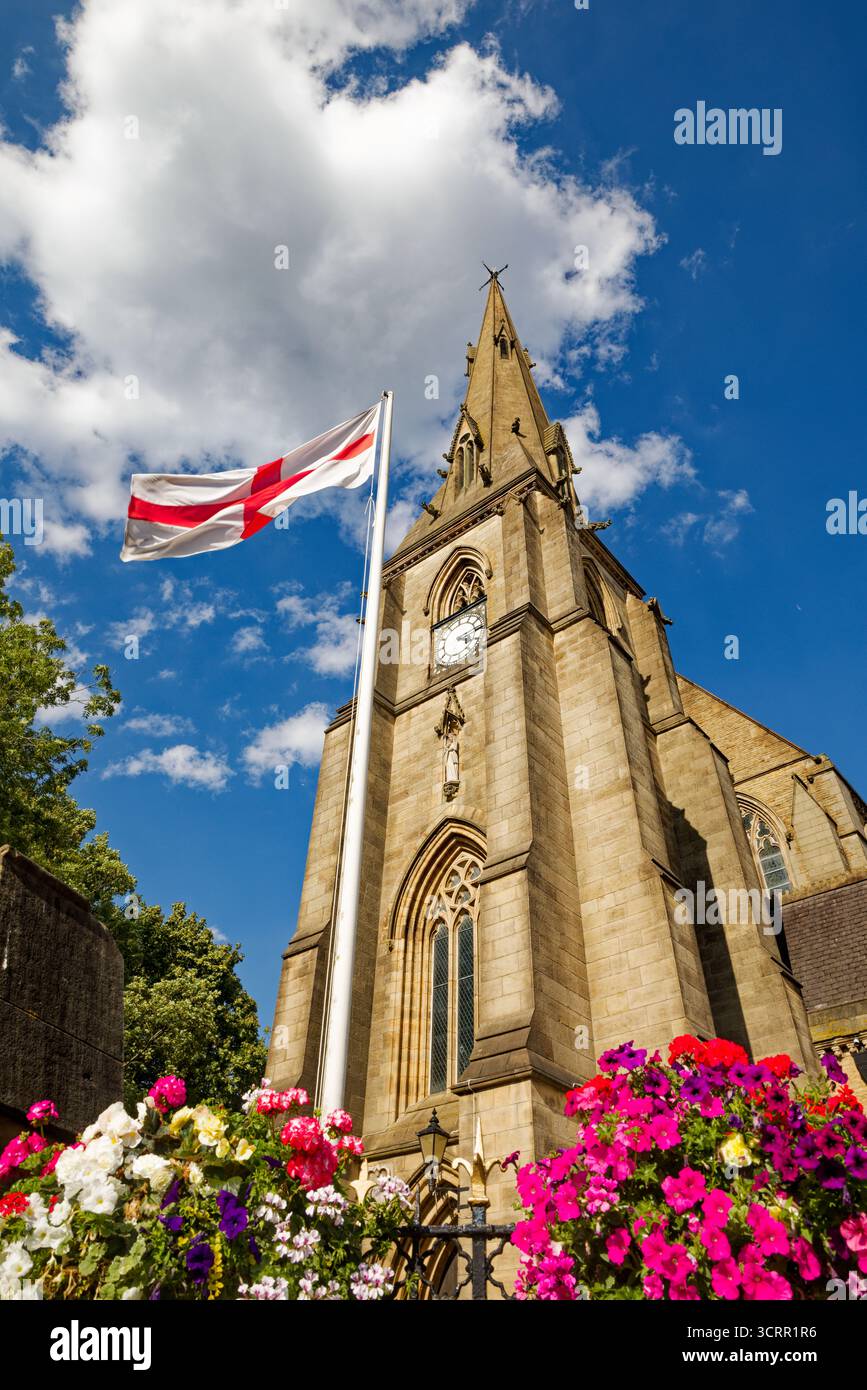 La guglia della chiesa parrocchiale si innalza in un cielo azzurro con un'esposizione colorata di fiori sotto una bandiera Union Jack, Bury, Greater Manchester. Foto Stock