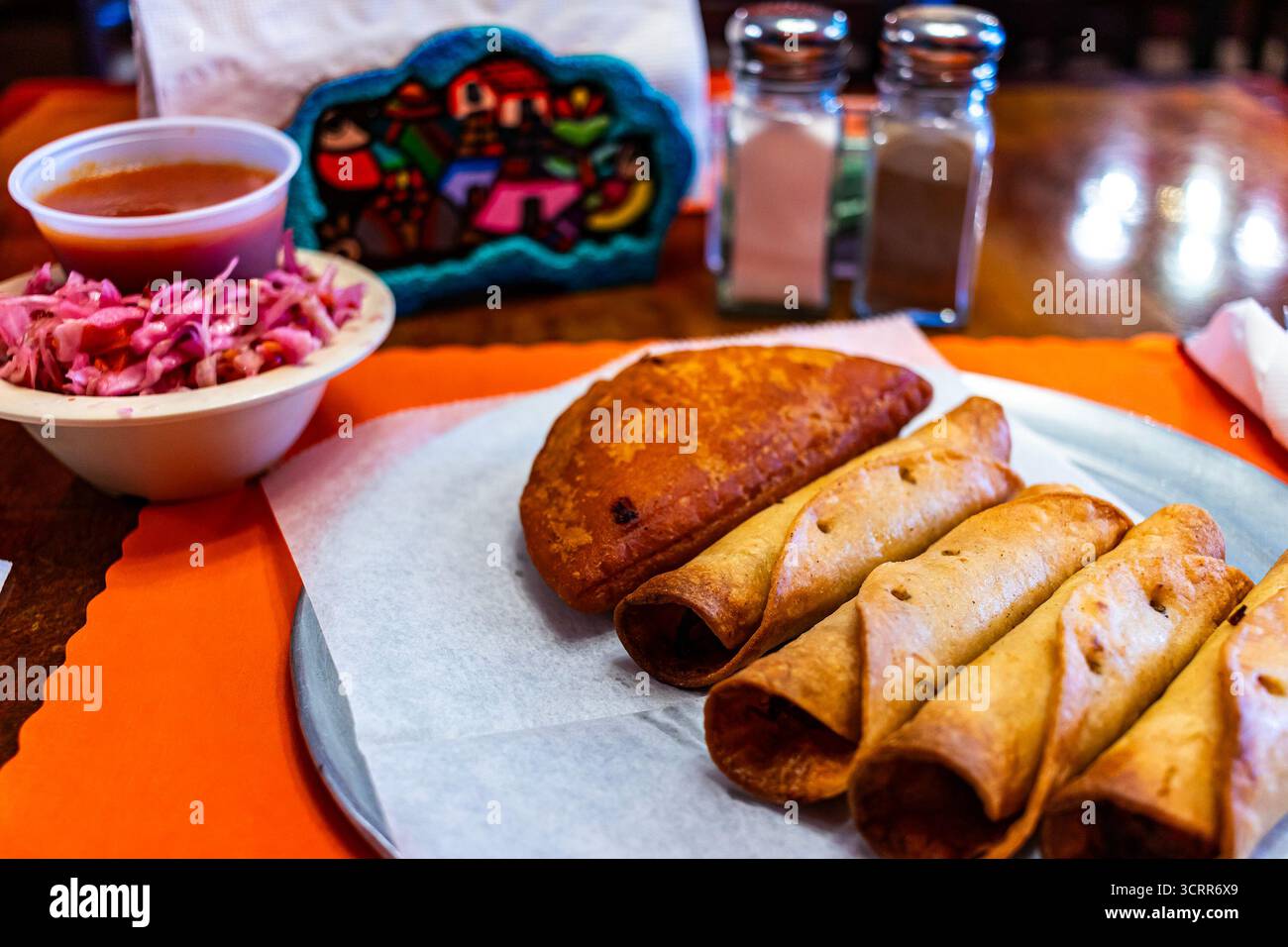 Tradizionale pasto salvadoregno con taquito fritto dorato e un'empanada croccante, servito con curtido (sciamano di cavolo sottaceto) e salsa di pomodoro Foto Stock