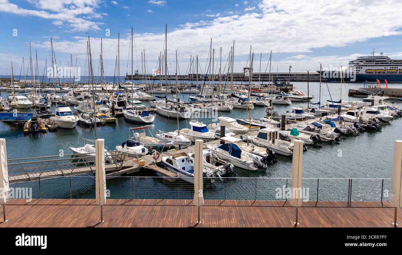 Un porticciolo con numerose barche e yacht attraccati, visto da un ponte di legno sotto un cielo parzialmente nuvoloso. Funchal Madeira Foto Stock