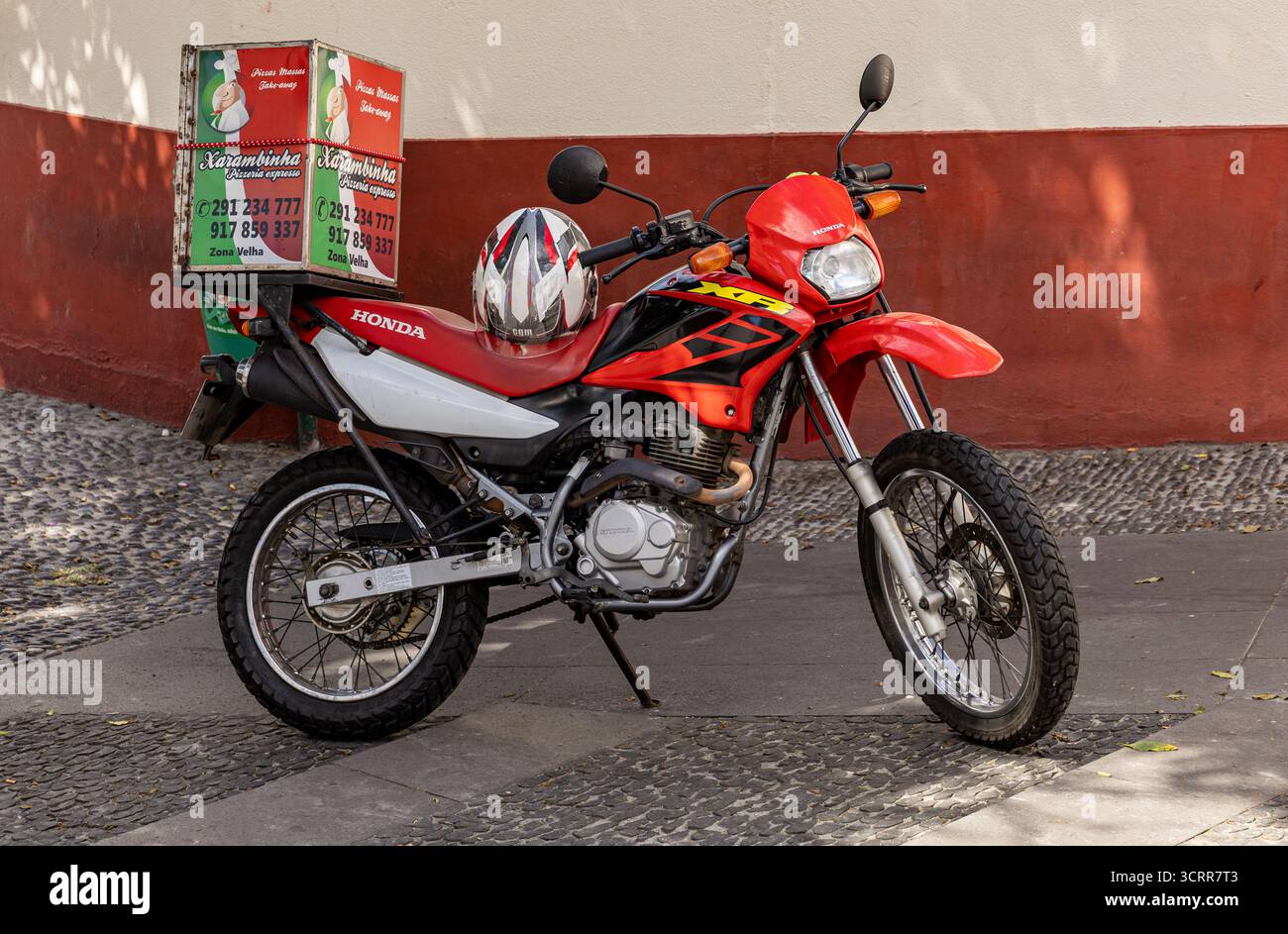 Moto Honda XR rossa parcheggiata su una strada cittadina a Funchal Madeira con una scatola di consegna e un casco poggiato sul sedile Foto Stock