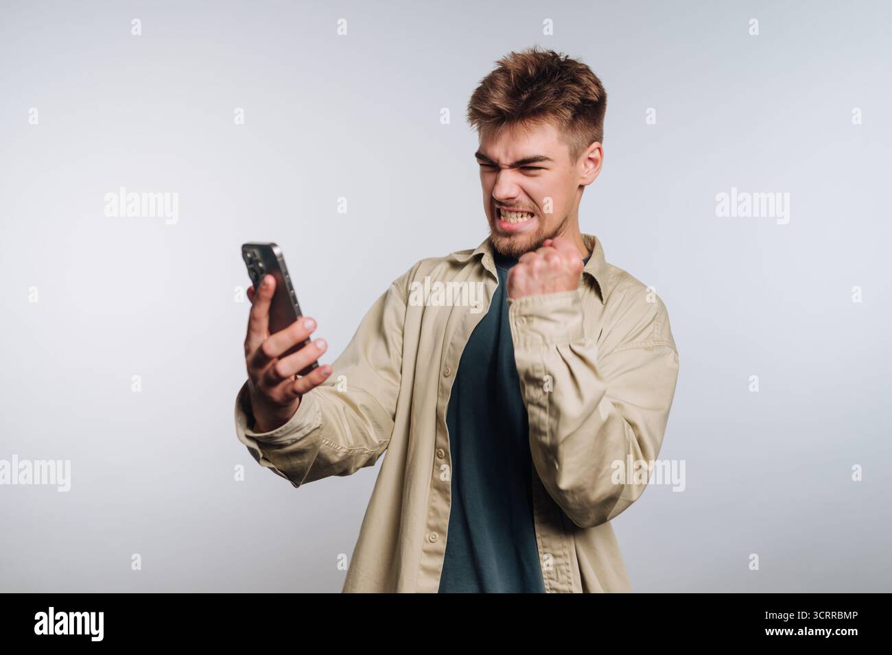 Un uomo frustrato che stringe il pugno mentre guarda il suo smartphone. Foto Stock