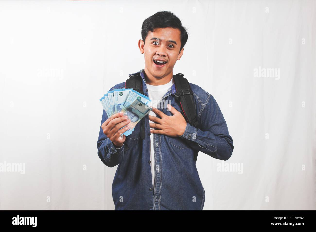 Giovane studente asiatico con uno zaino sorridente mentre tiene i soldi e si sente grato. Concetto di economia, successo, successo e libertà finanziaria. Foto Stock