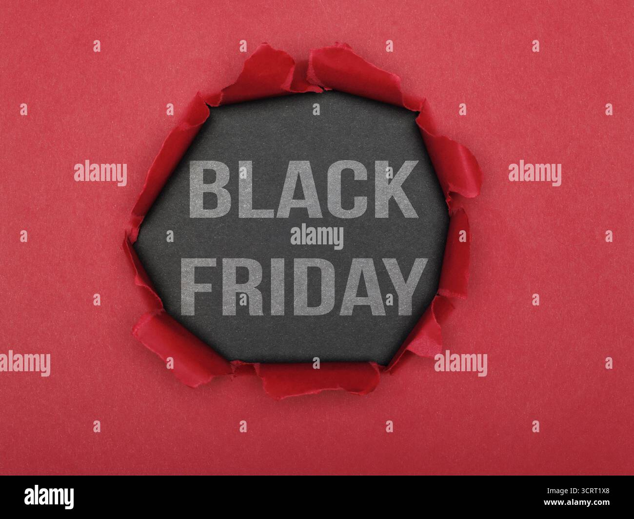 Un buco strappato in carta rossa che rivela uno sfondo grigio con le parole "Black Friday". Concetto di materiale pubblicitario e di marketing. Foto Stock