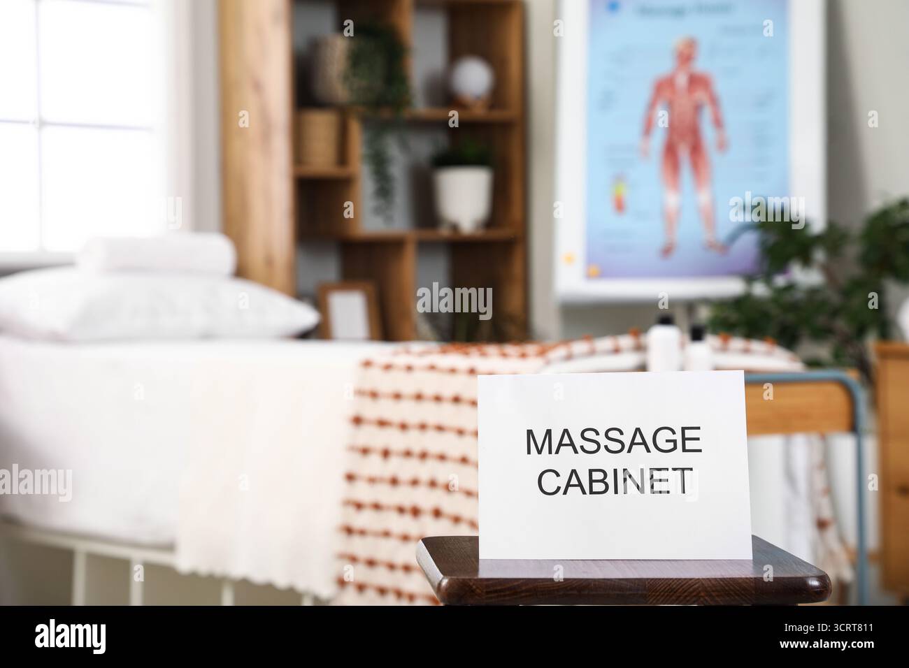 Scheda di carta con testo CABINA MASSAGGI sul tavolo vicino al divano del terapista nel moderno centro medico Foto Stock