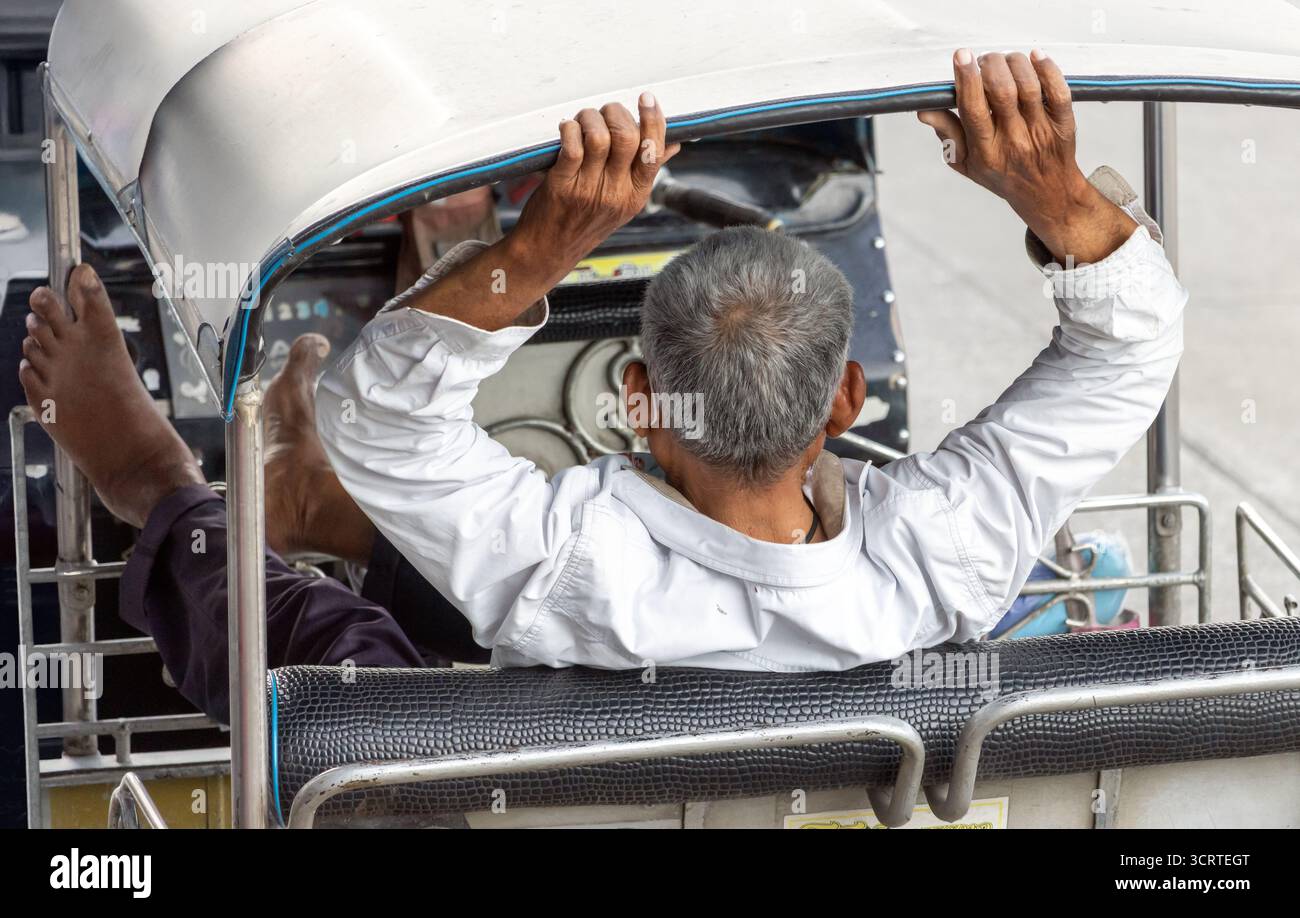 Un autista più anziano siede sui sedili posteriori di un triciclo tradizionale e aspetta i passeggeri, Bangkok, Thailandia Foto Stock