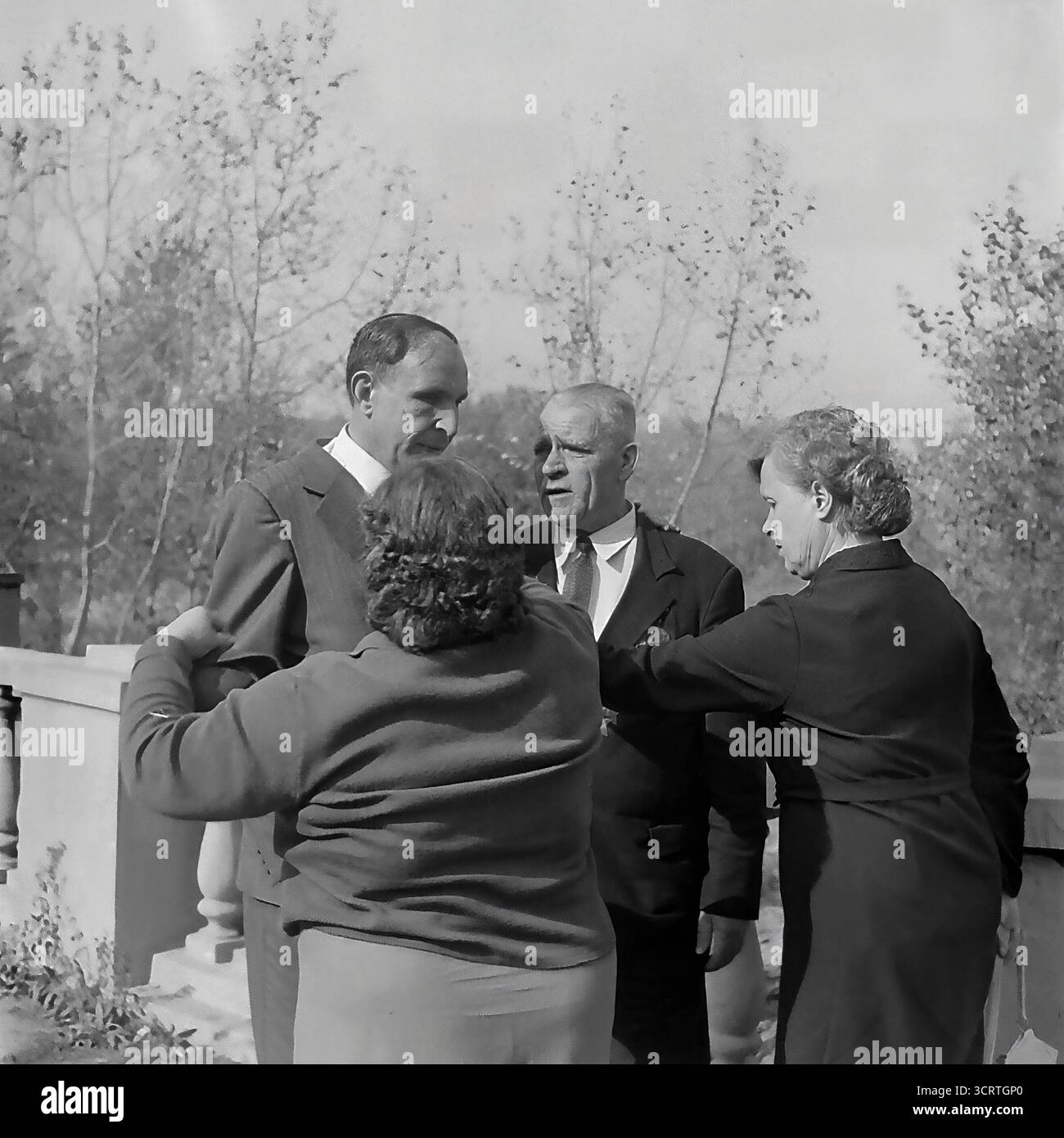Un'autentica fotografia d'archivio in bianco e nero del 1960 mostra un gruppo di funzionari e un veterano di guerra decorato a Sviatohirsk (allora Slavyanogorsk), RSS Ucraina. L'incontro si svolge su una terrazza all'aperto di un sanatorio o una "casa di riposo" nella famosa località turistica. Gli uomini e le donne sono impegnati in una conversazione rilassata ma formale. La presenza di un veterano della grande Guerra Patriottica (seconda guerra mondiale), la sua tuta decorata con medaglie, indica un evento ufficiale o commemorativo. Si tratta di un sincero assaggio della vita sociale delle figure rispettate dell'Unione Sovietica Foto Stock