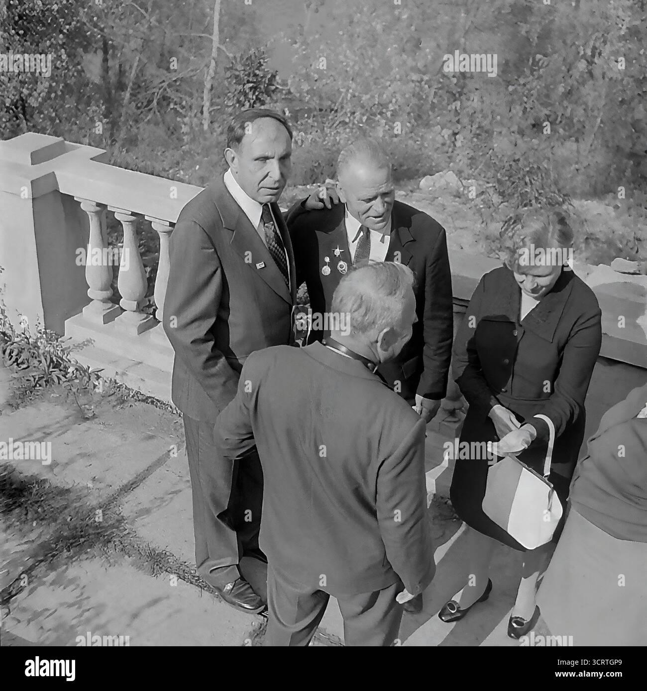 Un'autentica fotografia d'archivio in bianco e nero del 1960 mostra un gruppo di funzionari e un veterano di guerra decorato a Sviatohirsk (allora Slavyanogorsk), RSS Ucraina. L'incontro si svolge su una terrazza all'aperto di un sanatorio o una "casa di riposo" nella famosa località turistica. Gli uomini e le donne sono impegnati in una conversazione rilassata ma formale. La presenza di un veterano della grande Guerra Patriottica (seconda guerra mondiale), la sua tuta decorata con medaglie, indica un evento ufficiale o commemorativo. Si tratta di un sincero assaggio della vita sociale delle figure rispettate dell'Unione Sovietica Foto Stock