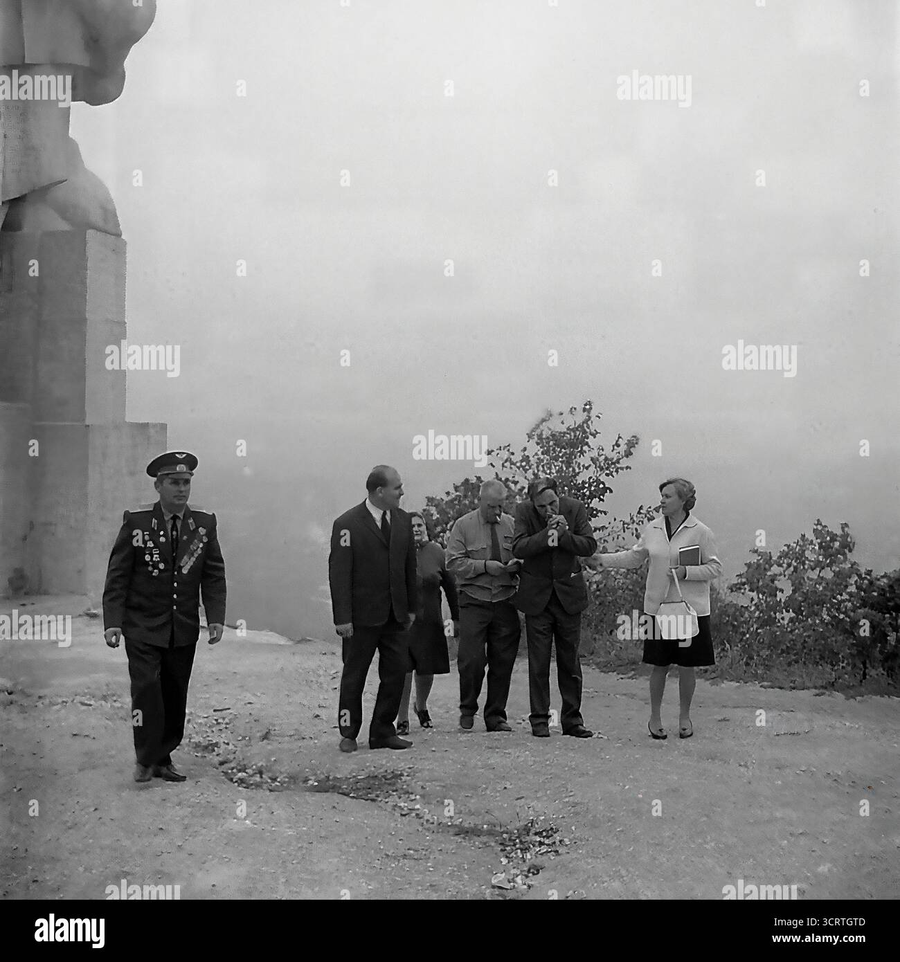 Una suggestiva fotografia d'archivio in bianco e nero degli anni '1960 mostra una delegazione ufficiale che visita il colossale Monumento ad Artem a Sviatohirsk, RSS Ucraina. Il gruppo, che include funzionari del partito e veterani di guerra decorati, cammina alla base della statua gigante. Progettato da Ivan Kavaleridze, il monumento è un capolavoro di arte sovietica famoso in tutto il mondo, eseguito in uno stile cubista/costruttivista unico. Questa immagine cattura un pellegrinaggio ufficiale verso uno dei monumenti ideologici più significativi della regione del Donbas e dell'intera URSS Foto Stock