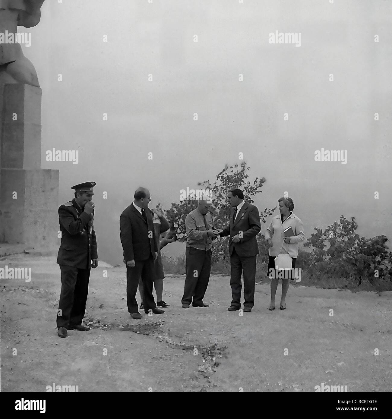 Una suggestiva fotografia d'archivio in bianco e nero degli anni '1960 mostra una delegazione ufficiale che visita il colossale Monumento ad Artem a Sviatohirsk, RSS Ucraina. Il gruppo, che include funzionari del partito e veterani di guerra decorati, cammina alla base della statua gigante. Progettato da Ivan Kavaleridze, il monumento è un capolavoro di arte sovietica famoso in tutto il mondo, eseguito in uno stile cubista/costruttivista unico. Questa immagine cattura un pellegrinaggio ufficiale verso uno dei monumenti ideologici più significativi della regione del Donbas e dell'intera URSS Foto Stock
