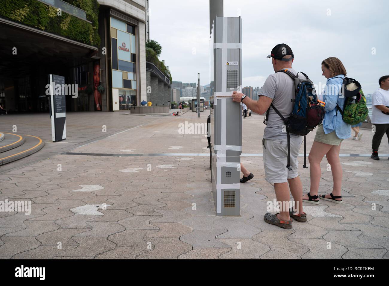Hong Kong, Cina - 23 settembre 2025: Un turista ispeziona la corda e il nastro utilizzati per assicurarsi un chiosco informativo all'aperto sulla Avenue of Stars Waterfr Foto Stock