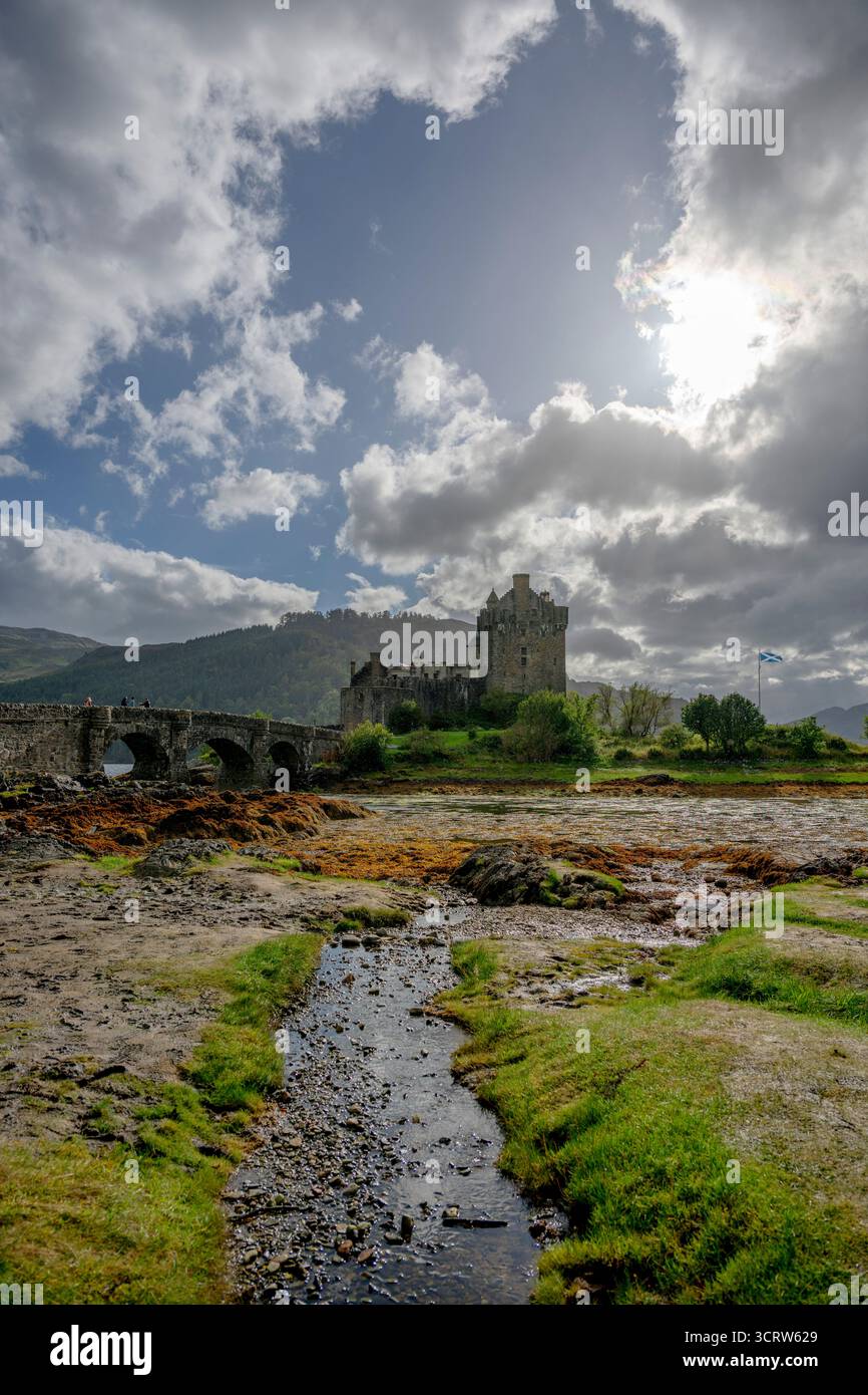 Il castello di Eilean Donan sorge su una piccola isola degli altopiani scozzesi raggiungibile da un ponte curvo, circondato da acqua, vegetazione e colline lontane. Foto Stock