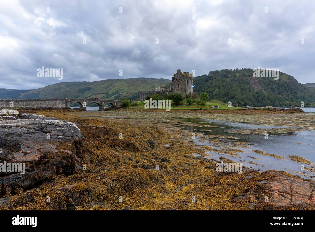 Il castello di Eilean Donan sorge su una piccola isola degli altopiani scozzesi raggiungibile da un ponte curvo, circondato da acqua, vegetazione e colline lontane. Foto Stock