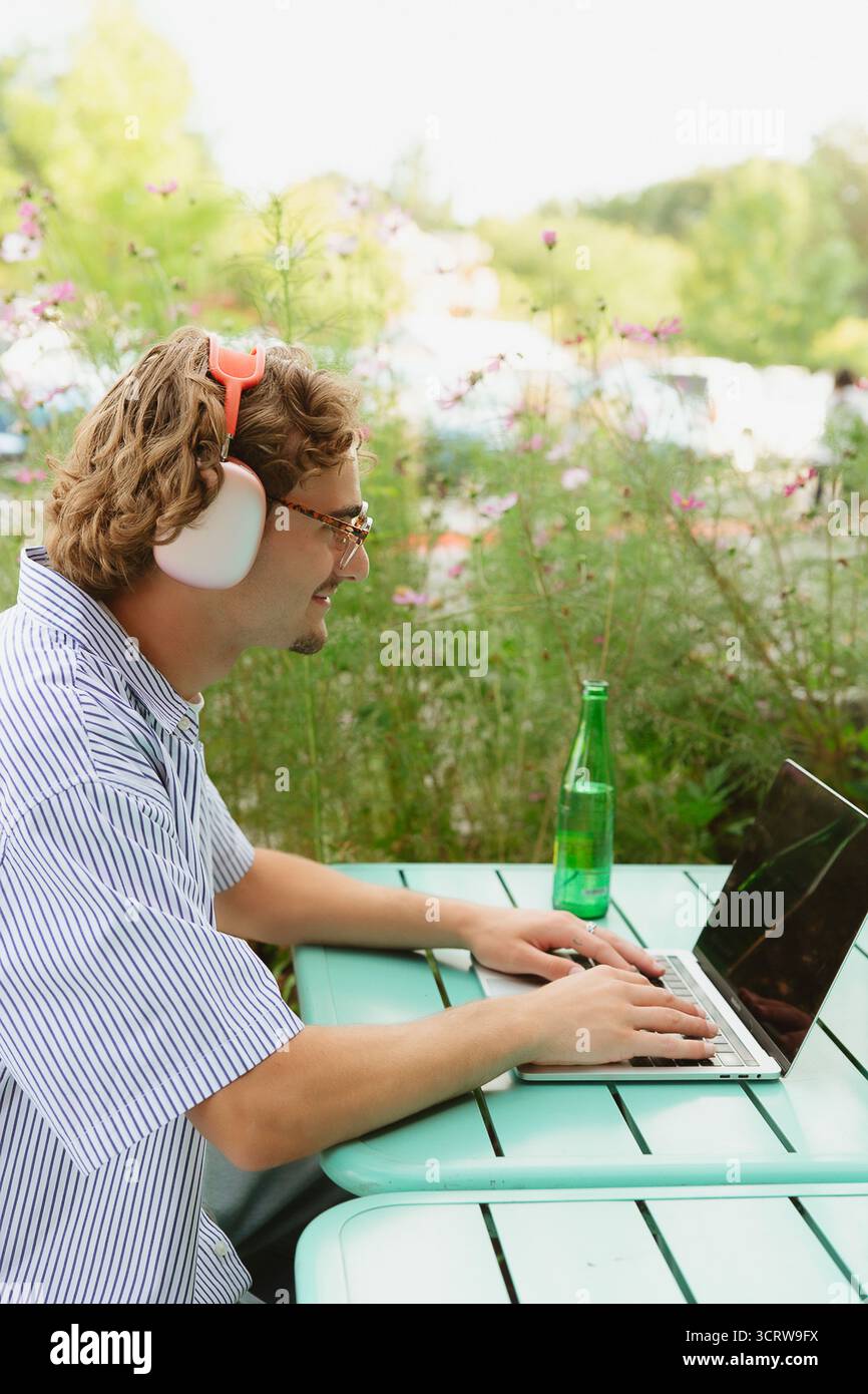 Uomo che indossa le cuffie che lavora con un computer portatile all'aperto in remoto Foto Stock
