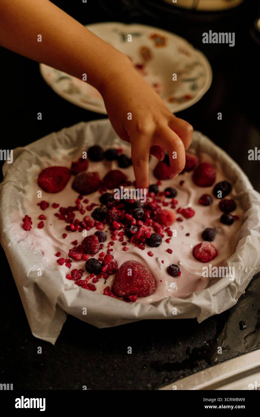 Aggiungere a mano frutti di bosco congelati su un cremoso dessert allo yogurt Foto Stock