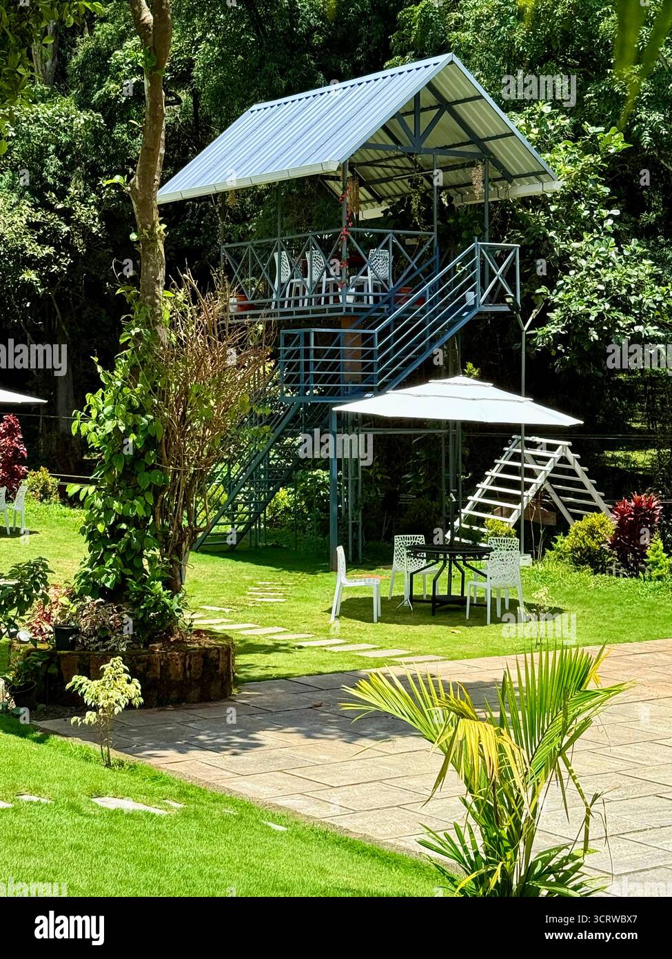 "Serene Garden Escape | Un incantevole gazebo all'aperto e una zona pranzo sopraelevata circondata da una vegetazione lussureggiante: Il luogo perfetto per rilassarsi, cenare o divertirsi - Immagine stock catturata con smartphone