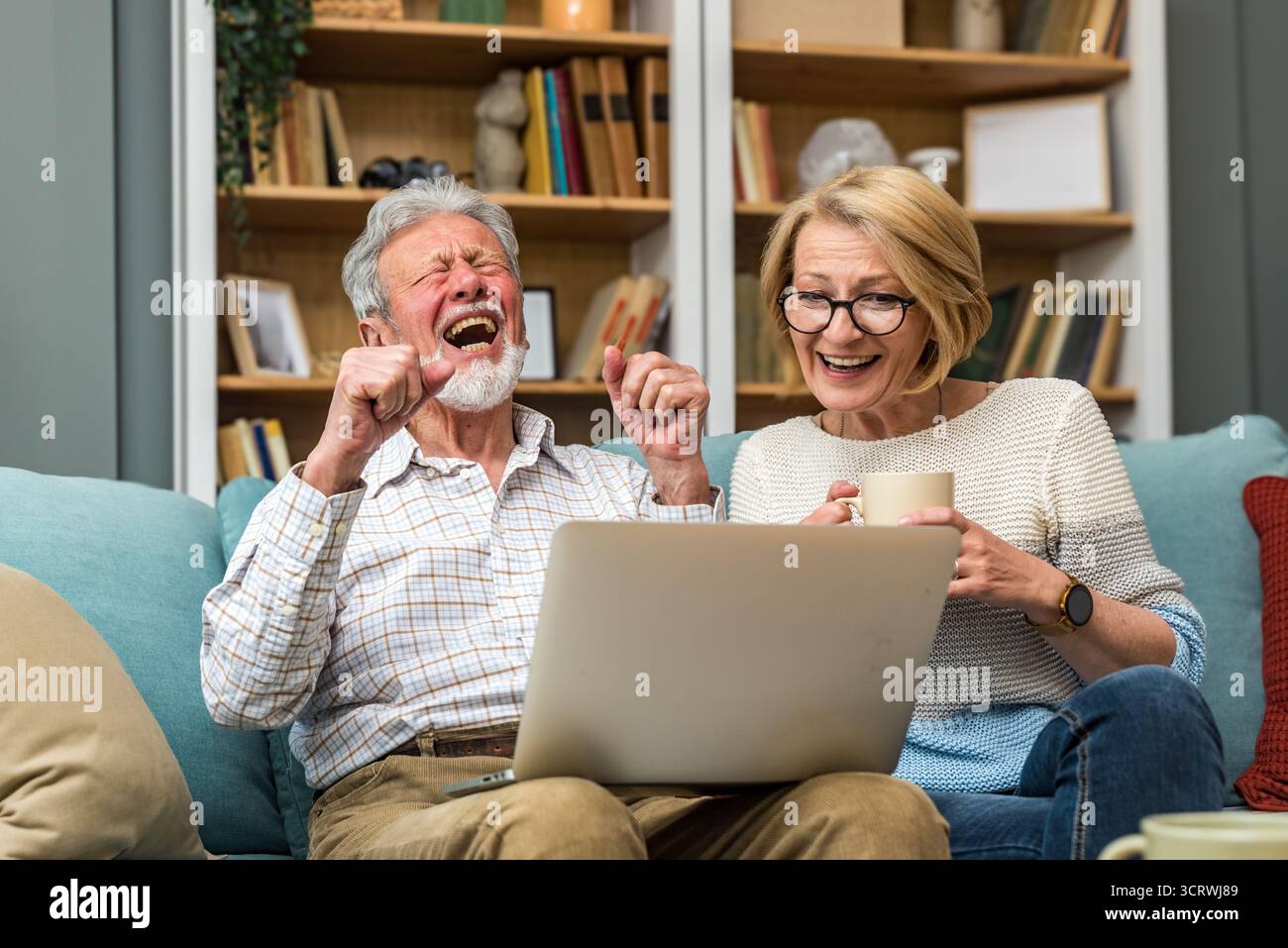 Coppia senior, anziani, vita semplice, seduti a casa sul divano, utilizzando la tecnologia per la prima volta, ordinando e facendo acquisti online su un computer portatile Foto Stock