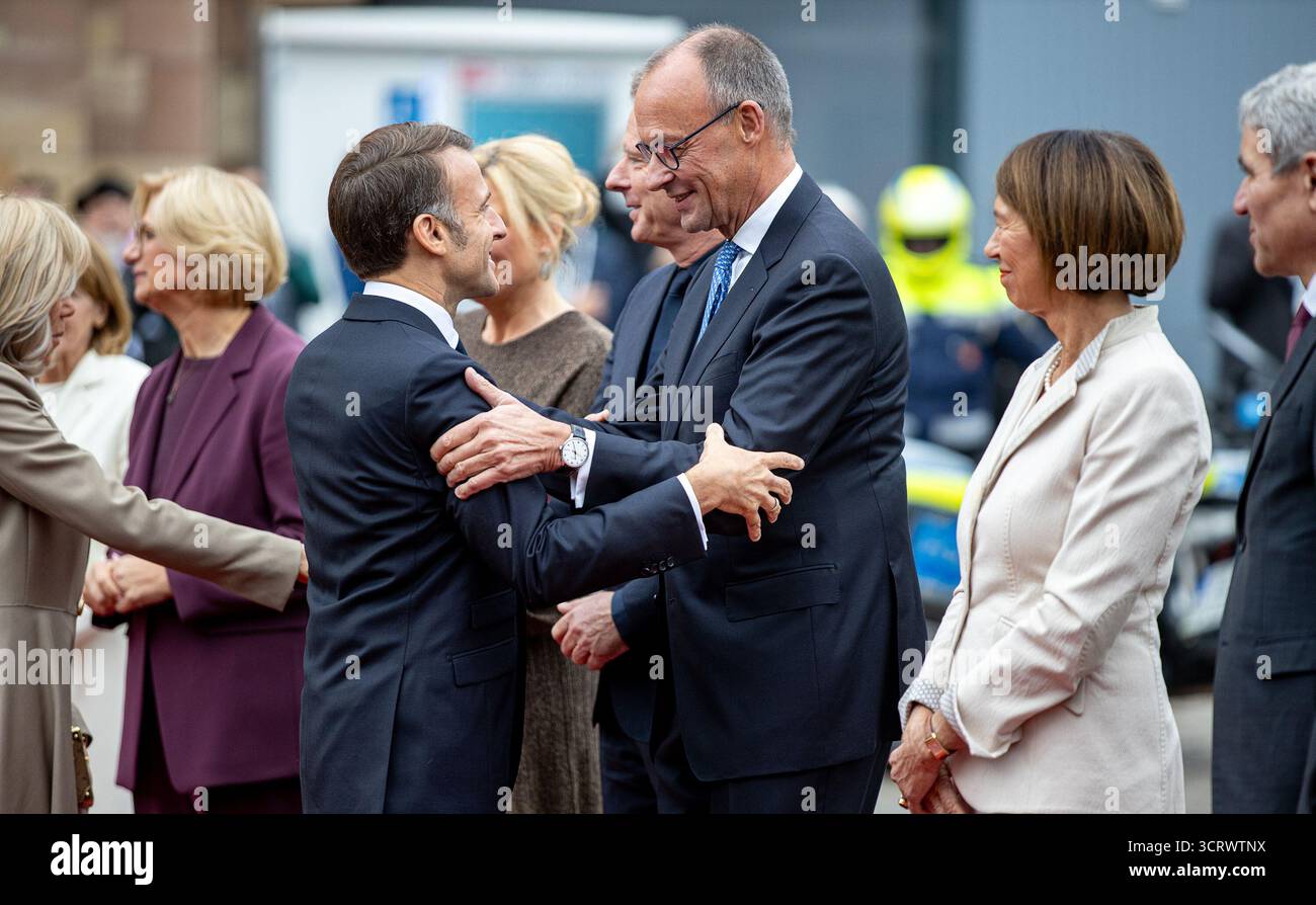 3 ottobre 2025, Saarland, Saarbrücken: Il presidente francese Emmanuel Macron (l) saluta il cancelliere federale Friedrich Merz (CDU) mentre arriva di fronte alla Cancelleria di Stato della Saarland durante le celebrazioni centrali per la giornata dell'unità tedesca; Charlotte Merz, moglie del Cancelliere federale, guarda avanti. Il 3 ottobre 2025, la Germania celebra il 35° anniversario della riunificazione tedesca. Foto: Pinter Laszlo/dpa Foto Stock