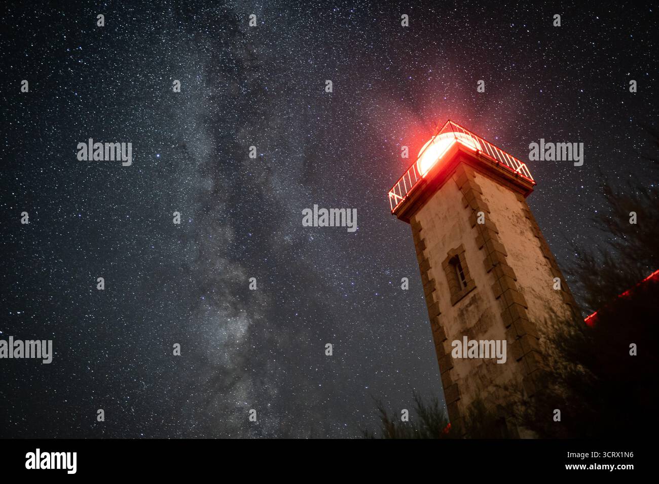 Una spettacolare foto a basso angolo di un faro che si illumina sotto la via Lattea, catturando la grandezza del cielo notturno e l'astrofotografia costiera. Foto Stock