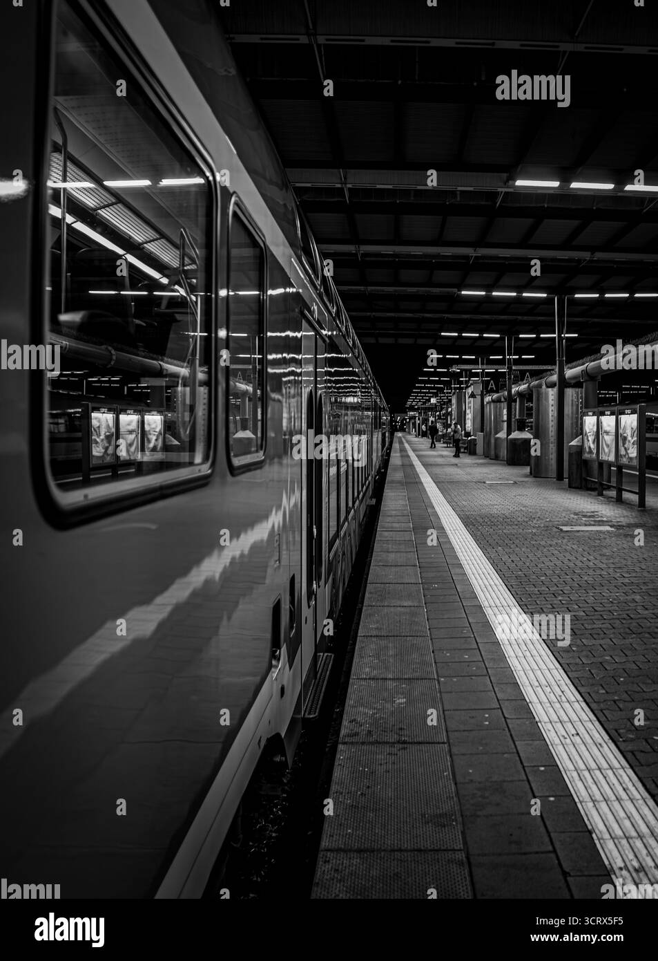 Una piattaforma ferroviaria silenziosa e vuota di notte, catturata in bianco e nero. Perfetto per progetti urbani, di viaggio o editoriali. Foto Stock