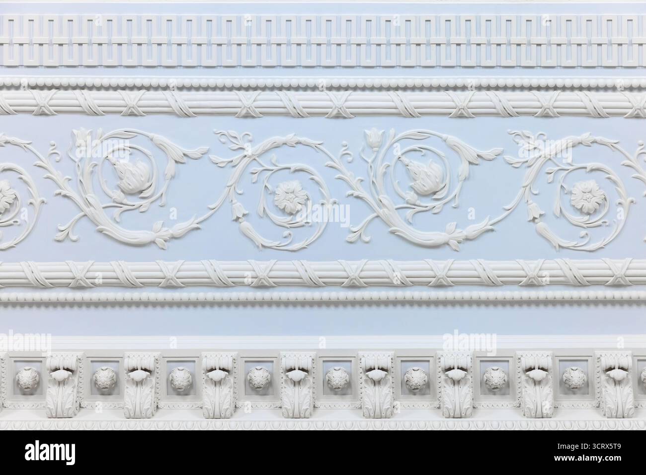 Intricati ornamenti in gesso bianco con viti floreali a scorrimento e rosoni adagiati su una parete blu pallido, caratterizzati da fregi a strati e decorazioni Foto Stock