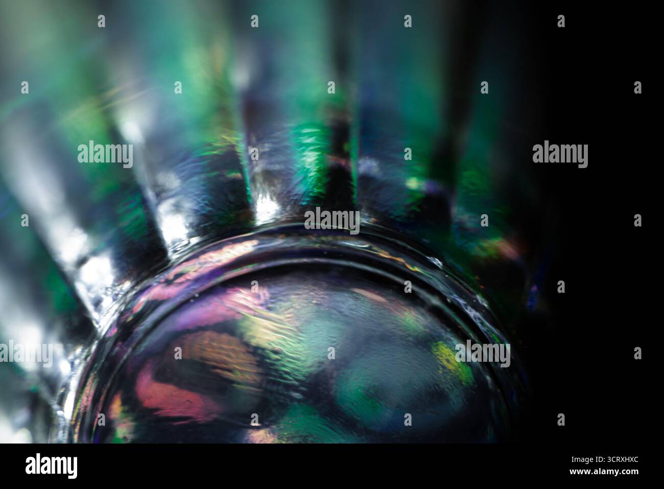 Foto macro di una superficie inferiore in vetro che mostra riflessi vividi e iridescenti, con sequenze di luce verdi, blu e viola che creano un effetto astratto e scintillante Foto Stock