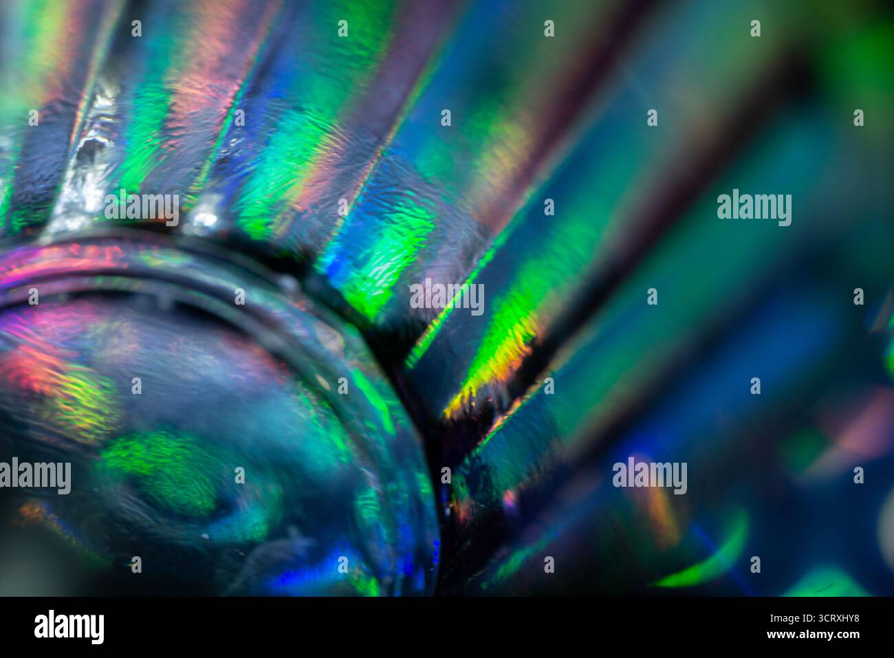 Foto macro di una superficie inferiore in vetro che mostra riflessi vividi e iridescenti, con sequenze di luce verdi, blu e viola che creano un effetto astratto e scintillante Foto Stock