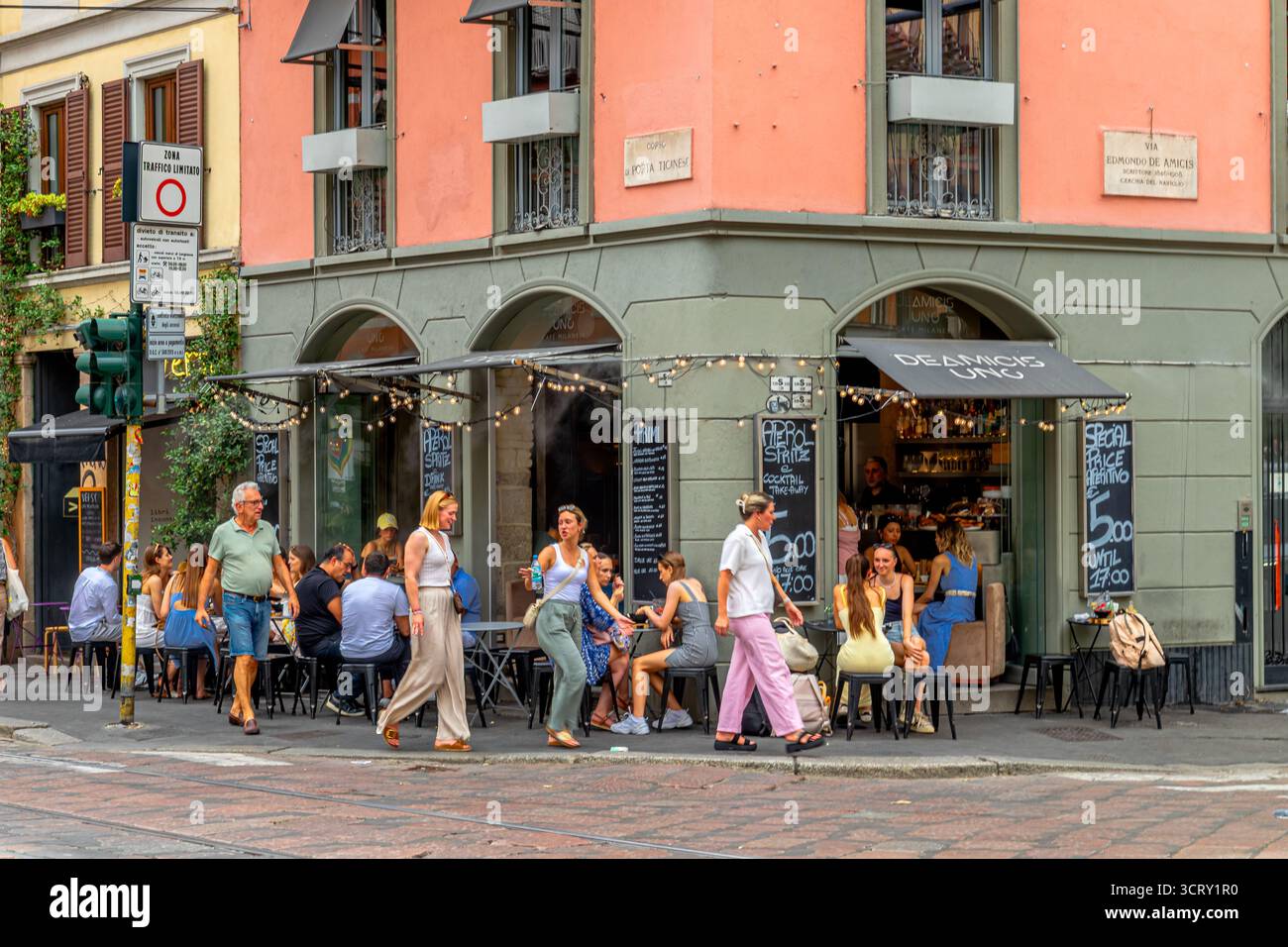 Le persone sedute fuori sul marciapiede si godono un drink al DeAmicis uno, un cocktail e un aperitivo bar in via Edmondo de Amicis, Milano, Italia Foto Stock