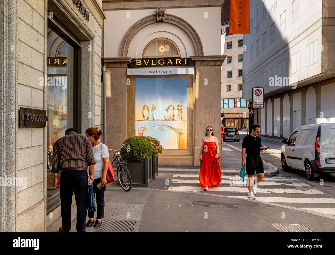 Una donna con un abito rosso e occhiali da sole passa davanti al negozio Bulgari in via Monte Napoleone, nell'esclusivo quartiere dello shopping di Milano Foto Stock
