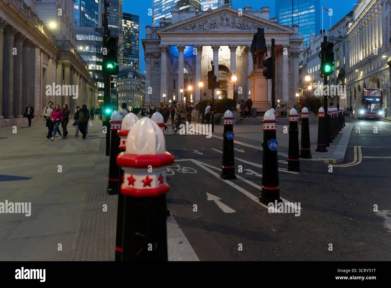 La gente passa davanti al Royal Exchange, Londra, al crepuscolo. Passa un autobus rosso a due piani. Foto Stock