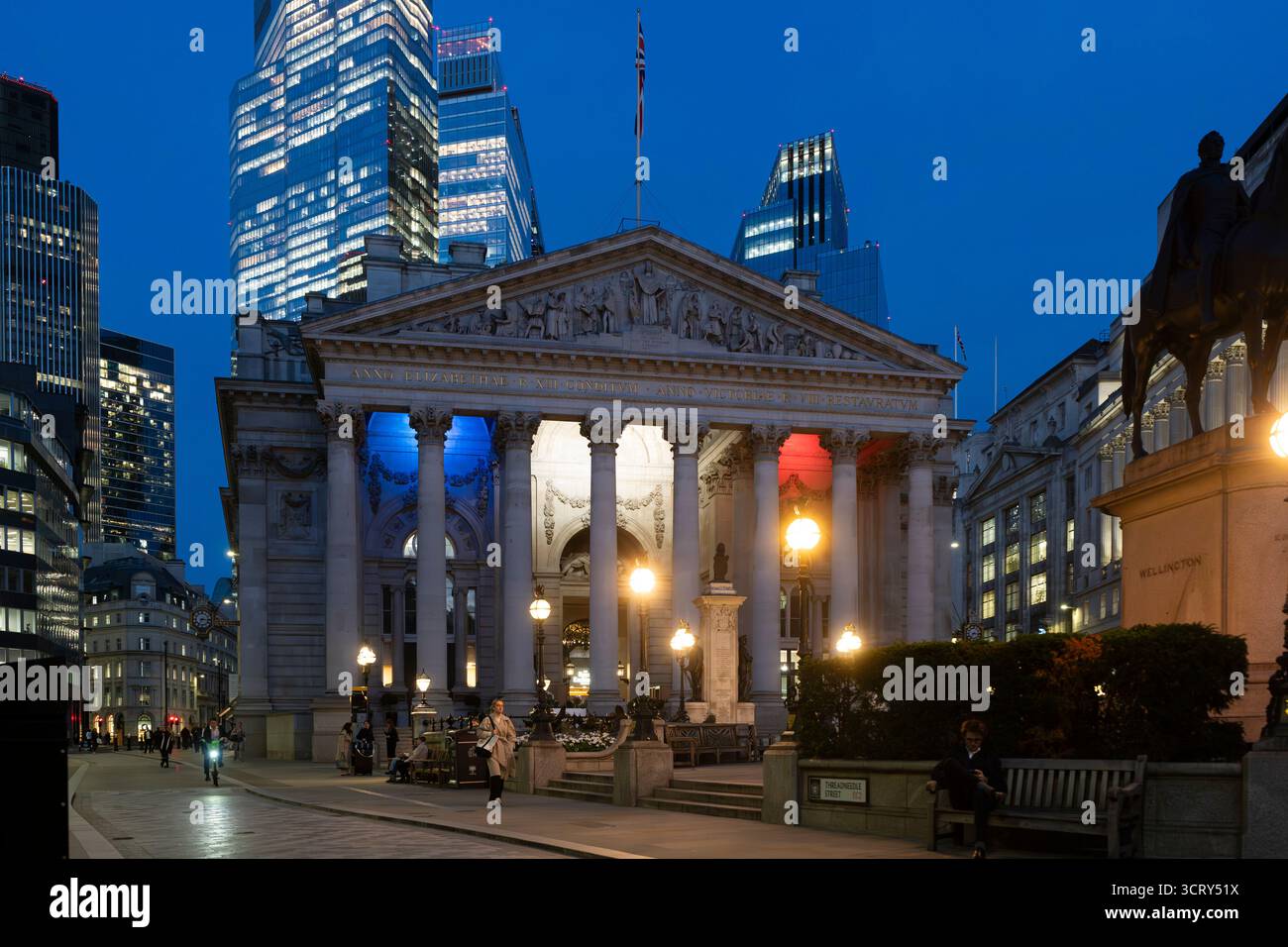 Il Royal Exchange di Londra, illuminato con la bandiera francese, si erge contro i moderni grattacieli. La gente passa al crepuscolo. Foto Stock