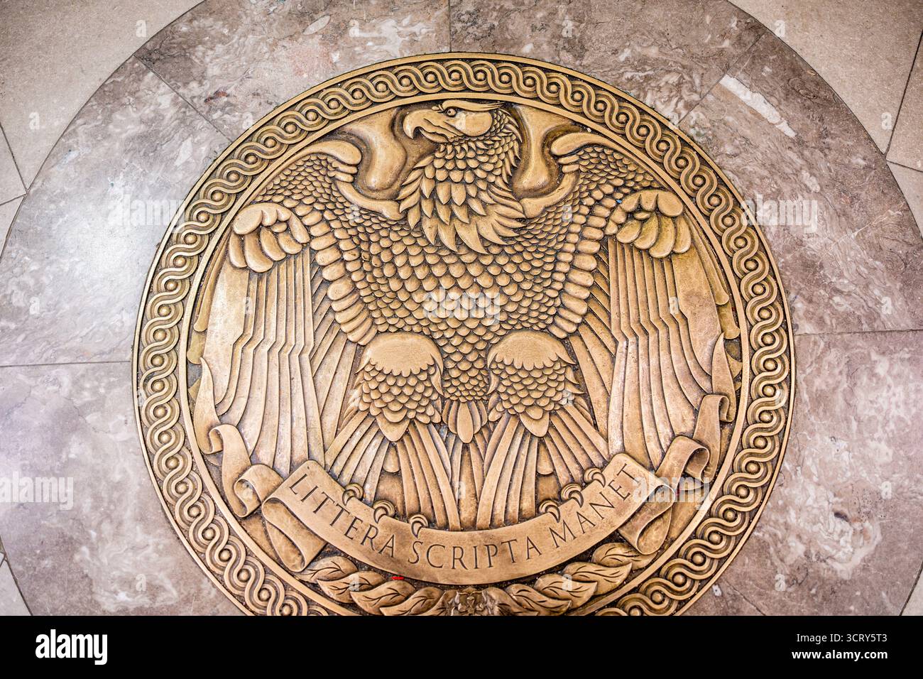 Medaglione di aquila in bronzo degli Archivi nazionali Washington DC | WASHINGTON D.C., Stati Uniti — Questa vista ravvicinata della medaglia di aquila in bronzo nell'atrio d'ingresso principale dell'edificio degli Archivi nazionali mette in evidenza il dettaglio stilizzato della piuma sotto il motto latino "Littera scripta manet", che significa "la parola scritta rimane". L'edificio degli Archivi nazionali sul National Mall ospita la Dichiarazione d'indipendenza, la Costituzione e il Bill of Rights. Foto Stock
